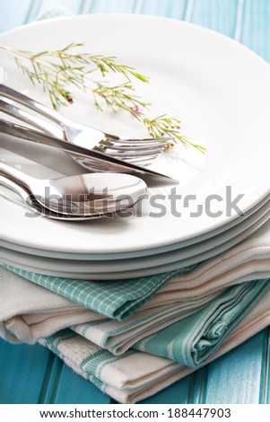 A stack of clean white plates with silverware on blue napkins