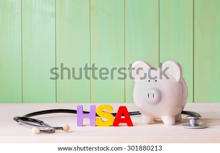 Health Savings Account HSA concept with white  piggy bank, stethoscope wood block letters and green background