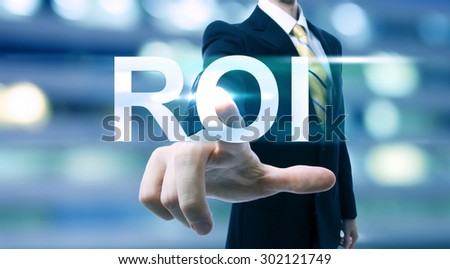 Businessman pointing at ROI (return on investment) on blurred city background