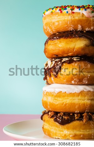Stack of assorted donuts on a white plate on pastel blue and pink background