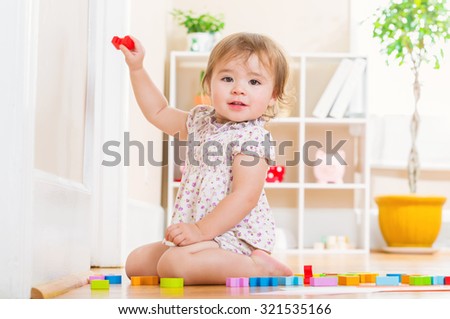 Happy toddler girl smiling and playing with her toy blocks inside her house
