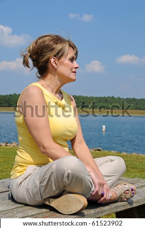 Attractive Mature Woman sitting on a Picnic Table by the Lake