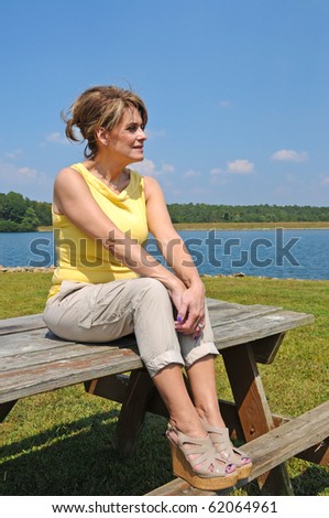 Attractive Mature Woman sitting on picnic table by the Lake