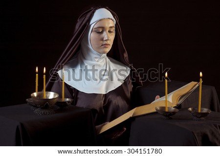Young beautiful woman nun reading bible on black  background. Through the candles. Low-key lighting.