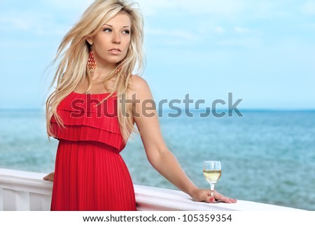 beautiful sexy girl in red dress and a glass of wine by the sea