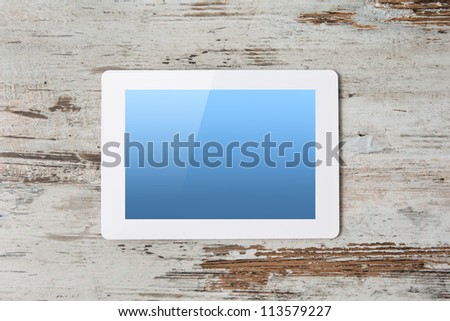 white tablet touch computer gadget with blue screen on a background of wood.