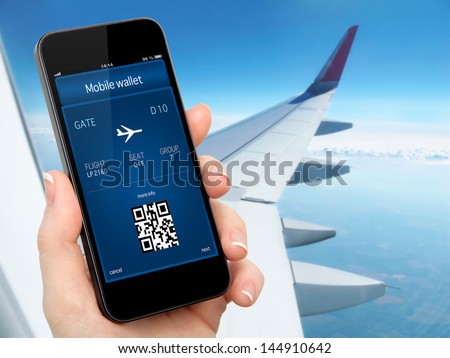 woman hand holding the phone with mobile wallet and plane ticket against the background of the window with blue sky and airplane wing