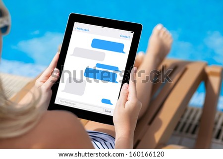 girl in a bathing suit lying on a sun lounger by the pool with a computer tablet with sms chat on a screen