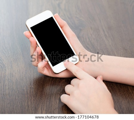 female hands holding a white touch phone with a black screen on a wooden table