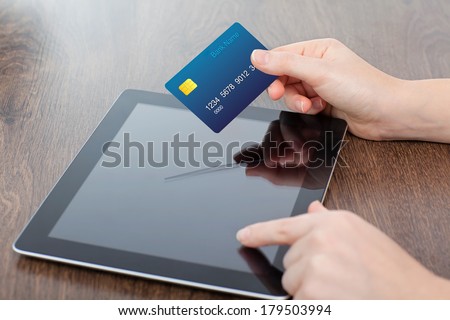 female hands holding credit card and a computer tablet on the table in the office
