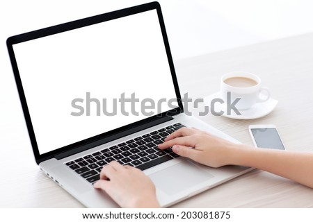 Female hands typing on a laptop keyboard with isolated screen in a white room on a desk with a phone and a cup of coffee