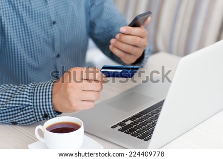 man makes the payment by credit card on the laptop and holding phone