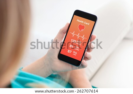 woman sitting on the sofa and holding a phone with app for health card monitoring
