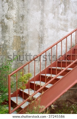 exterior detail of a back-alley red metal staircase against a grungy wall
