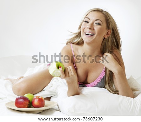 Young laughing woman lying in bed with apples
