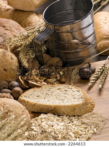 An assortment of whole grain breads with mixed nuts and seeds on a table. An old time sifter sits in the background