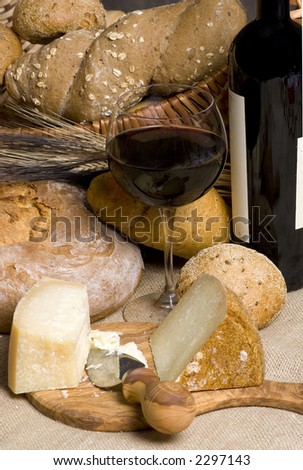 A glass of red wine with an assortment of breads and cheeses