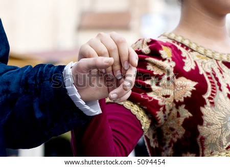 A couple holds hands as they walk down the entrance to an elegant dinner.