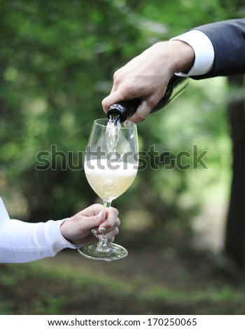 Man serves white wine to his woman glass in the green park, wedding event, outdoor picnic