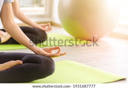 Time for practicing yoga. Two youngs attractive women sitting in Ardha Padmasana exercise, Lotus pose on meditation, closed eyes, wearing sportswear on mat at home. lifestyle concept