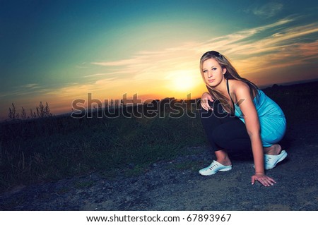 Young sporty woman crouching on a road in sunset