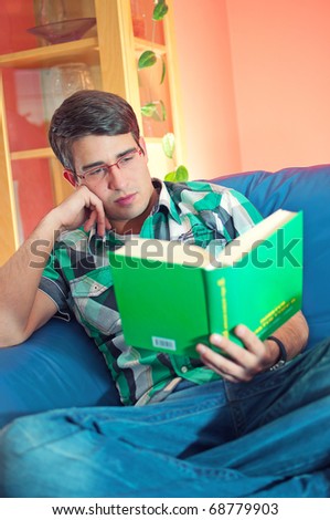 A handsome student with glasses relaxing with a book on a couch