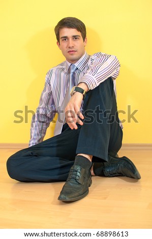 Portrait of a relaxed young businessman sitting on the floor and resting against uniform background