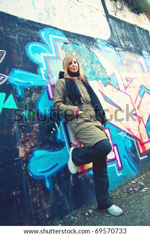 Beautiful young woman standing by the road in front of graffiti wall