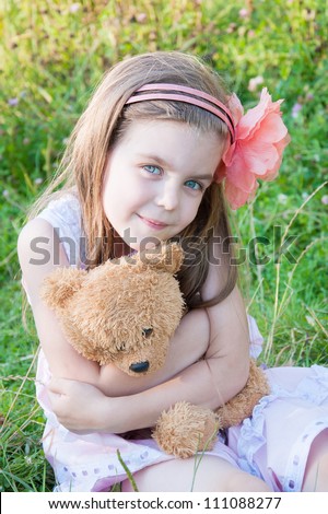 Happy little girl hugging a teddy bear  against summer nature.