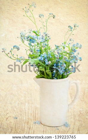 Bouquet of forget-me-not flowers in  a white vase on a grunge  background