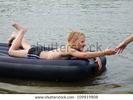 The child on an inflatable mattress gives a hand, in reply to given a hand of adult person