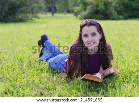 The beautiful young woman lies on a grass in a summer garden with the book