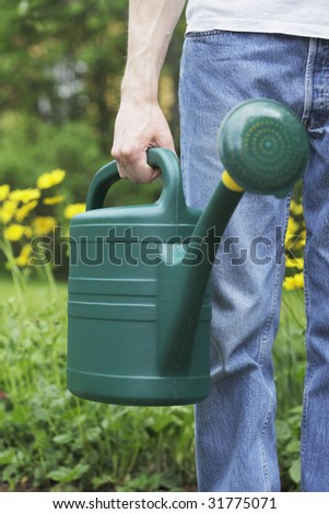 A Man holding a green plastic watering can in his hand. Short depth of field, sharpness is in the hand.