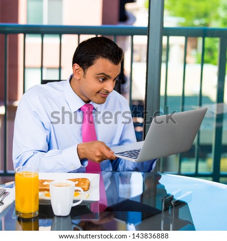 Closeup portrait of surprised shocked stunned handsome businessman eating breakfast and looking browsing on his laptop screen device, sales price, project, email, isolated on city background
