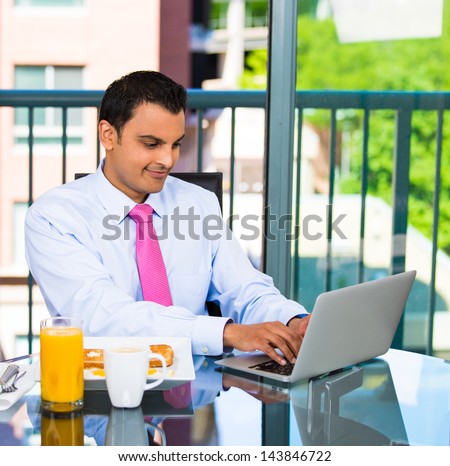 Portrait of handsome businessman or student eating breakfast and happily typing and working on his laptop, isolated on city background with trees