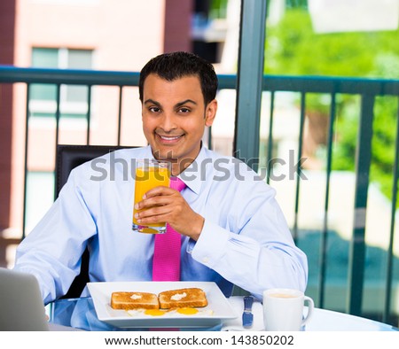 Handsome young businessman or student, smiling, eating healthy breakfast toast and eggs, coffee, juice and working on laptop, isolated on a city background with trees