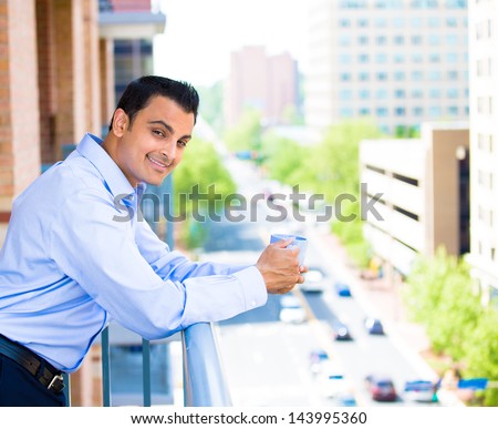 Closeup portrait of young man enjoying a drink while standing outside on his balcony, isolated on city background