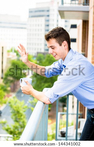 Handsome man leaning on rail, waving from balcony, and enjoying drink, isolated on city background with trees and buildings