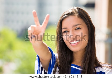 A close-up picture of a beautiful happy woman giving a victory sign relaxing on a summer day on a balcony of a new apartment, on a city background