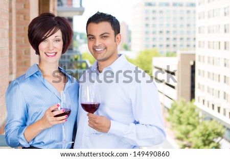 Portrait of man and woman toasting wine on outside balcony, isolated on a city background with trees