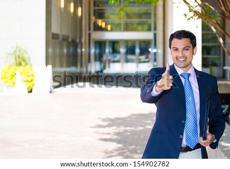 Closeup portrait of handsome businessman in suit giving thumbs up sign on a sunny day, isolated on a city urban background.