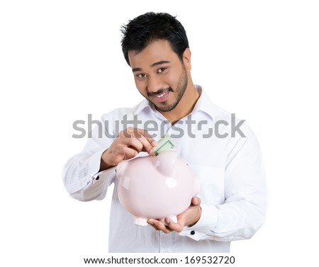 Closeup portrait of young smiling man school student worker guy holding piggy bank depositing money coins into piggy bank, isolated on white background. Smart financial investment decisions.