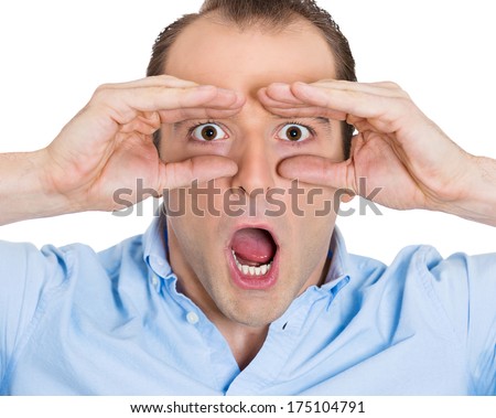 Closeup portrait of young, curious guy, funny man, looking through his fingers like binoculars, searching for something, surprised shocked by what is waiting him in future isolated on white background