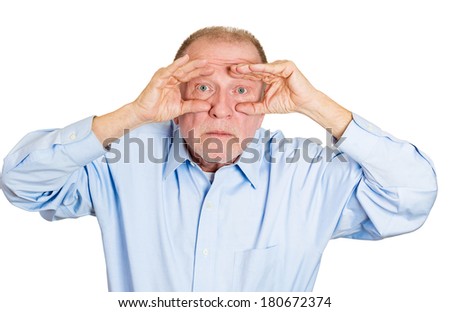 Closeup portrait of senior mature serious man peeking through his fingers like binoculars, searching for something, looking to the future at the camera, isolated on a white background. Sign, symbols
