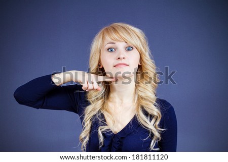 Closeup portrait angry young woman gesturing with hand to stop talking, cut it out,  she will take your head off, isolated dark blue background. Negative emotion, facial expressions, feeling, attitude