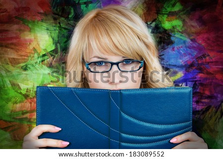 Closeup portrait nerdy, shy, young student girl, woman with blue glasses hiding behind book, reading isolated colorful kaleidoscope background. Face expression, emotions, attitude, reaction, education
