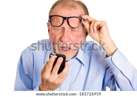 Closeup portrait, senior mature man, nerd black glasses, having trouble seeing cell phone screen because of vision problems. Bad text message. Negative human emotion facial expression feelings.