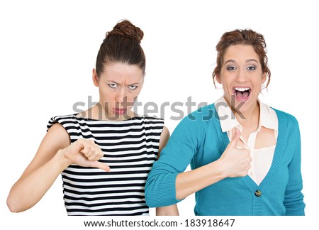 Closeup portrait, two young people, women. One being excited happy smiling, showing thumbs up, other serious, concerned, unhappy showing thumbs down, isolated white background. Emotion contrasts
