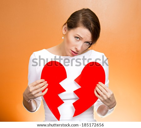 Closeup portrait young, troubled, sad, confused woman, holding broken heart in hands, about to cry, isolated orange background. Negative human emotions, facial expression, feelings, attitude, reaction