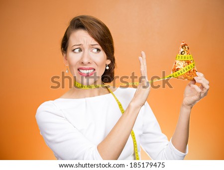 Closeup portrait sad, young, confused woman holding, looking at fatty pizza with measuring tape around, trying to withstand, resist temptation to eat it isolated orange background.  Facial expression